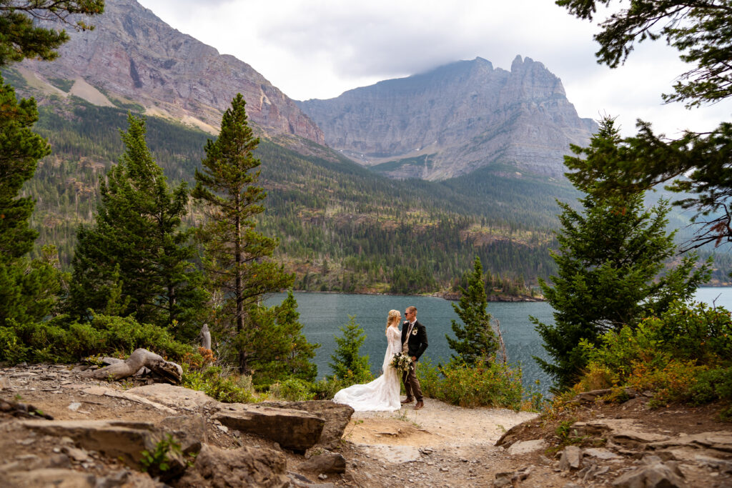 Bride and groom looking at one another on the shore of glacier lake in Glacier National Park.