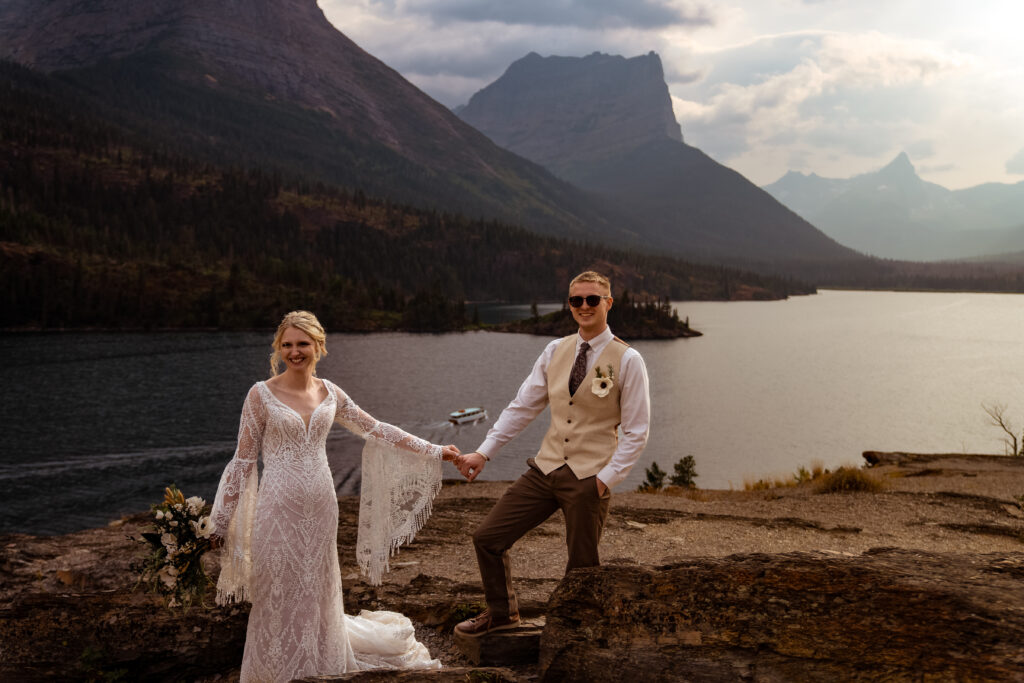 Elopement image showing a couple on a cliff above a lake with a boat passing by.
